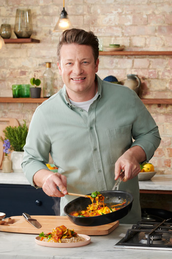 Jamie Oliver präsentiert lächelnd eine Pfanne in der Küche